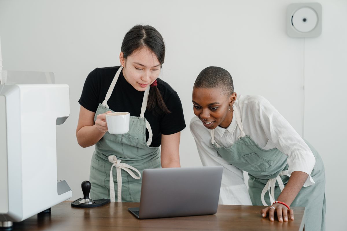 Two café workers in aprons looking at a laptop together
