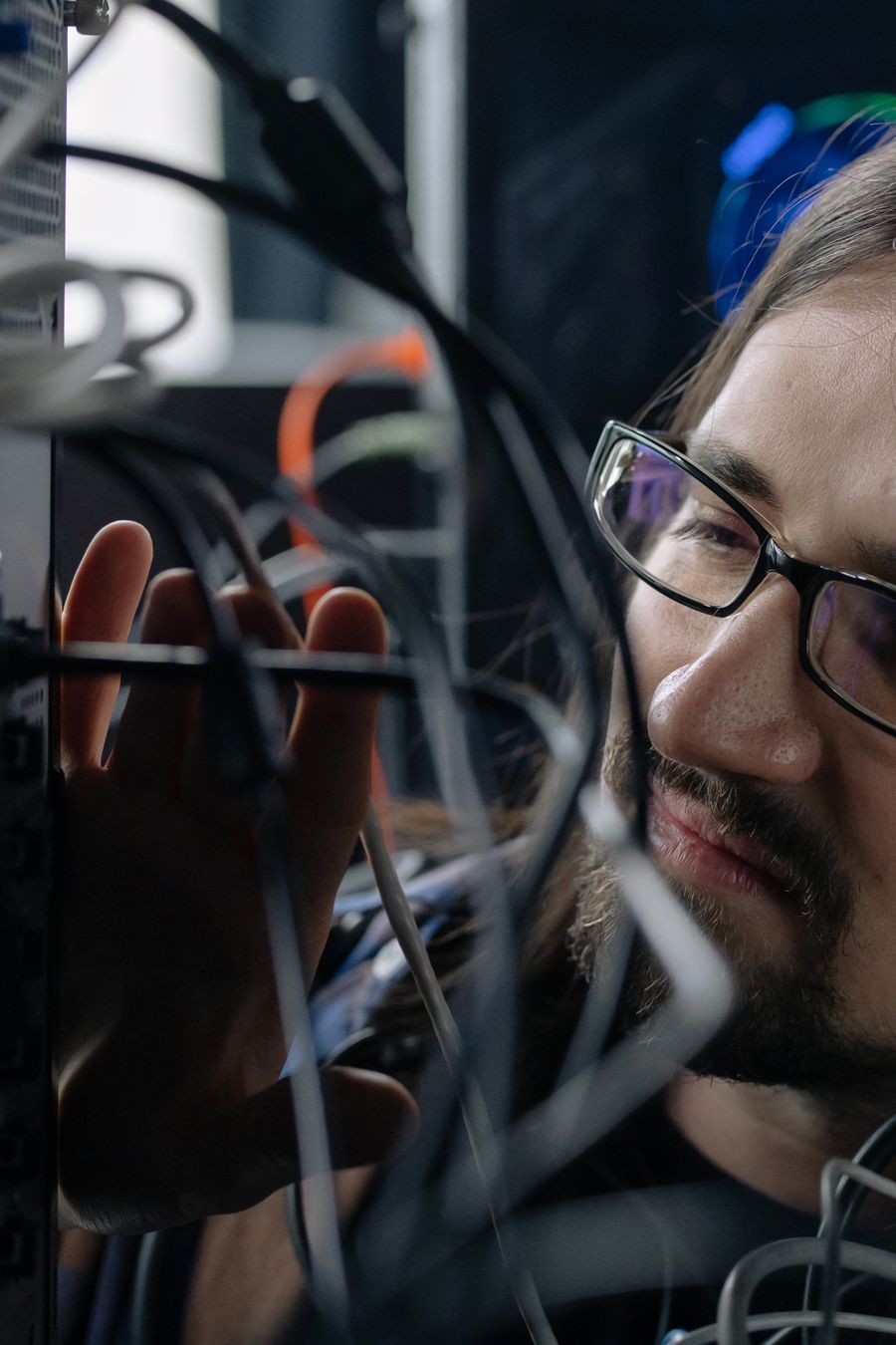 A technician in glasses peering into a cabinet of network cables