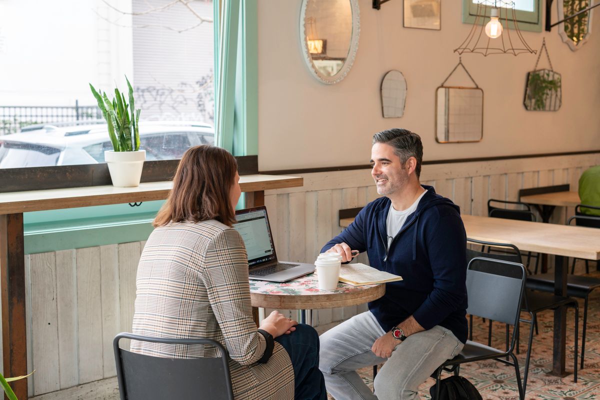 Two people talking over a laptop in a café