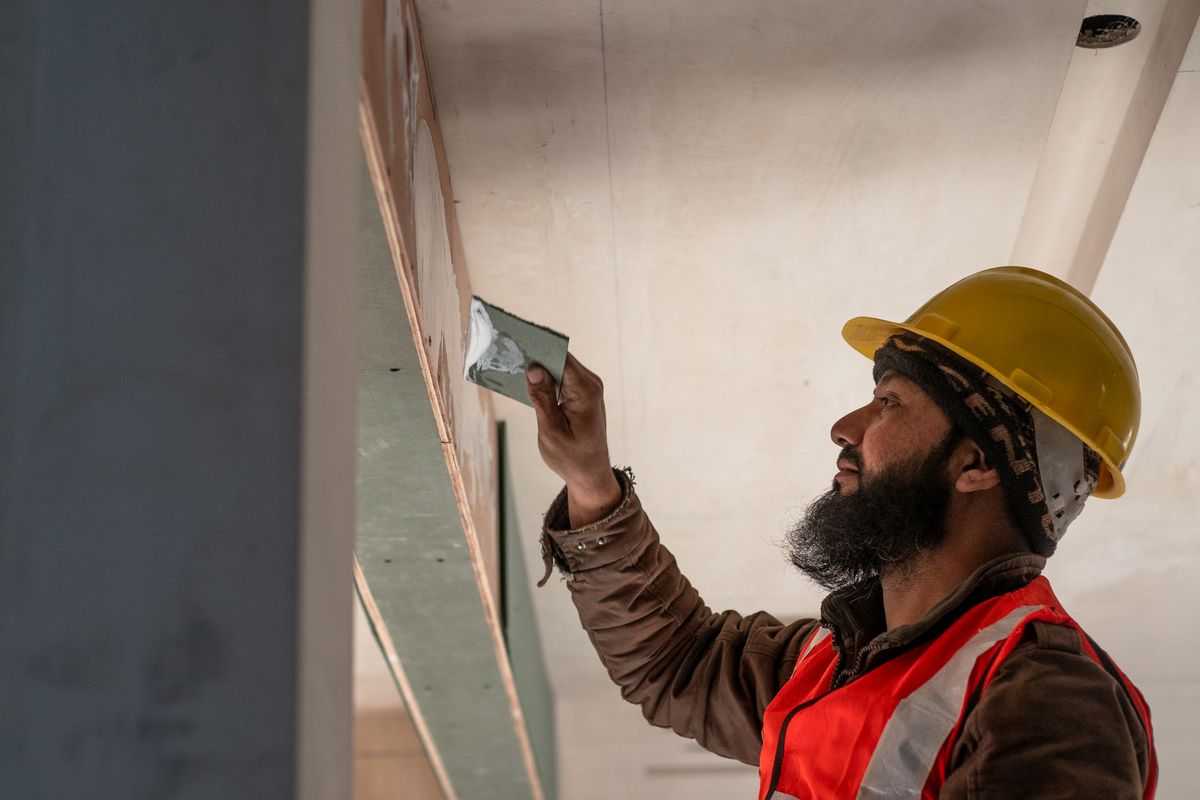 A worker in a hard hat and high visibility vest skimming a wall on site