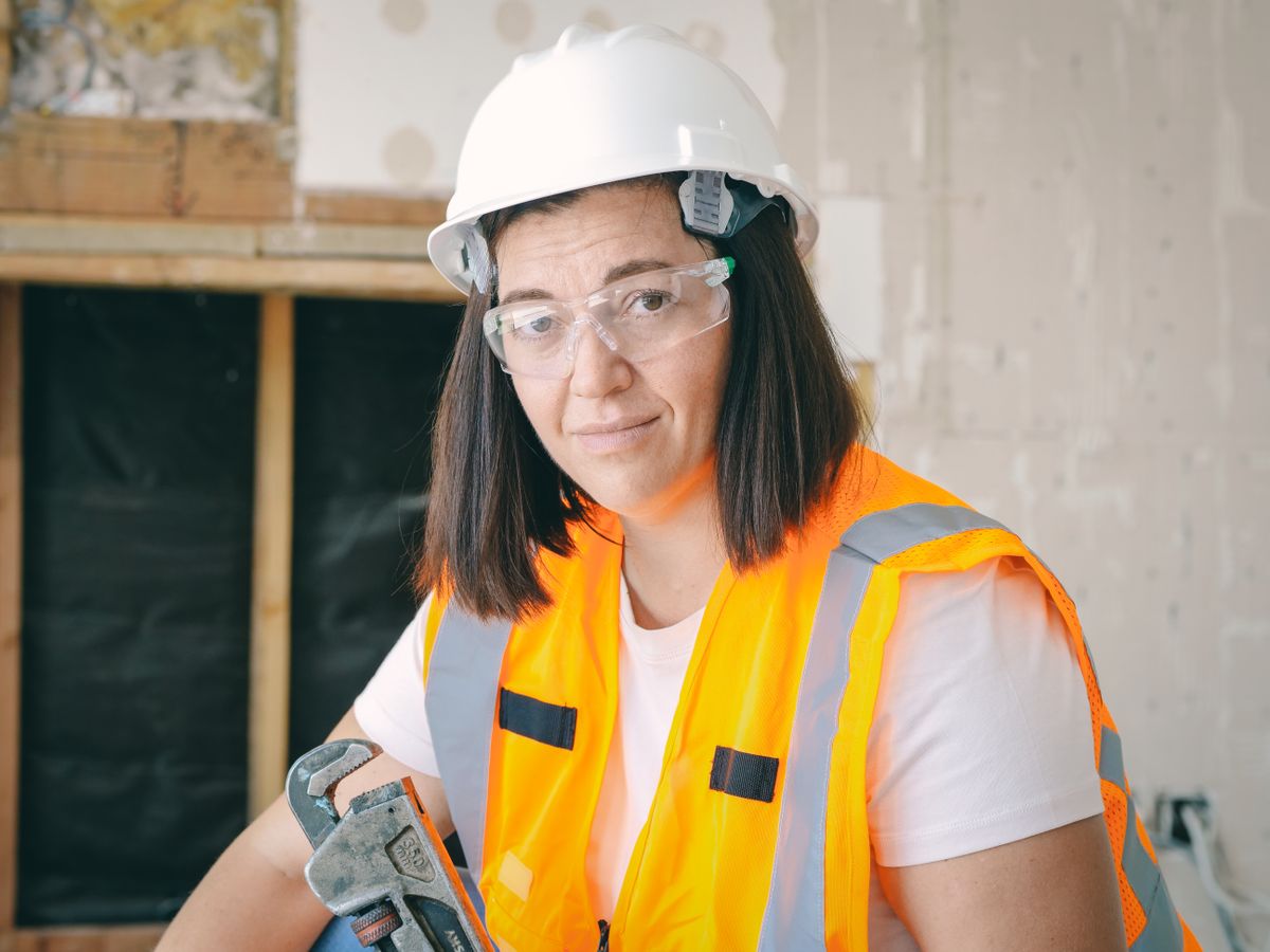 A worker in a hard hat and high visibility vest in a stripped interior with exposed studs