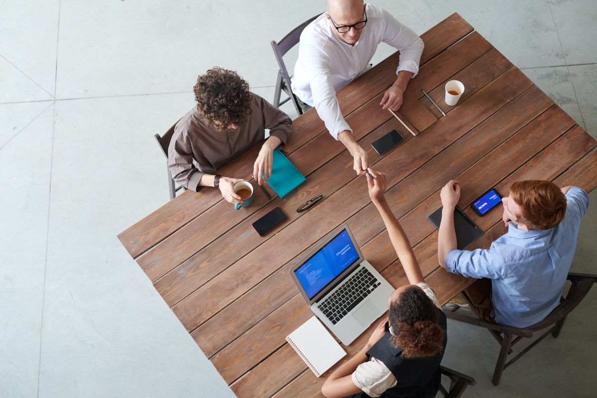 Four people at a wooden table with laptops, seen from above