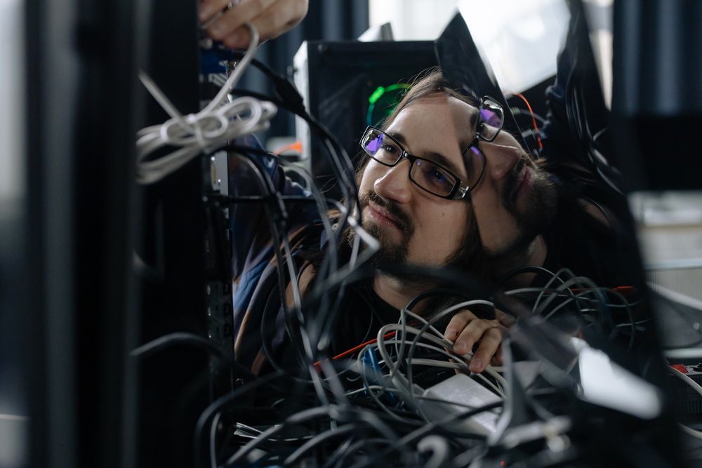 The same technician under a desk, working through a tangle of cables